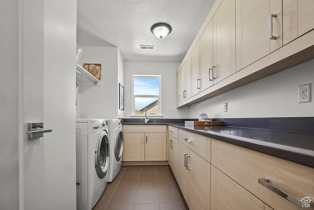 Clothes washing area with washing machine and dryer, dark tile patterned flooring, a textured ceiling, and cabinet space