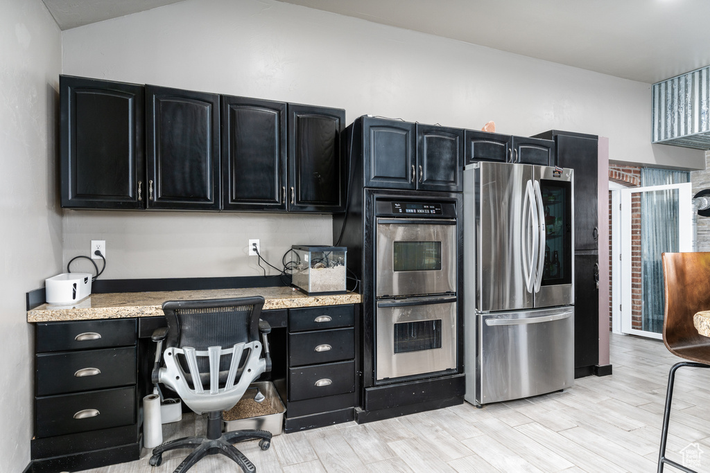 Kitchen featuring stainless steel appliances, dark cabinets, light wood-style floors, and lofted ceiling