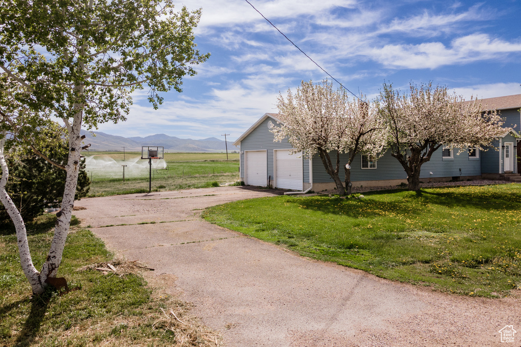 View of property exterior with asphalt driveway, a garage, a lawn, and a mountain view