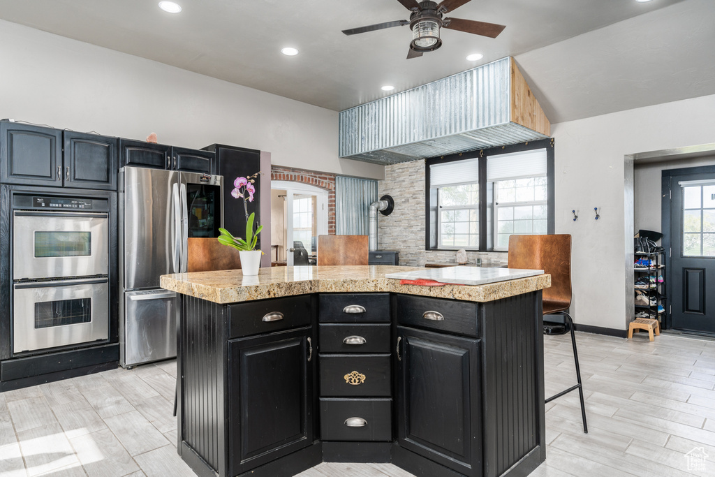Kitchen with stainless steel appliances, a center island, light countertops, dark cabinets, and a ceiling fan