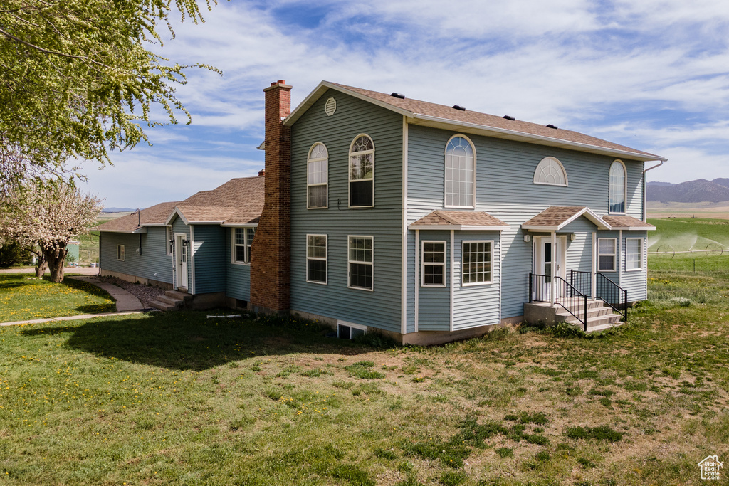 Back of house with a lawn, a chimney, and a shingled roof