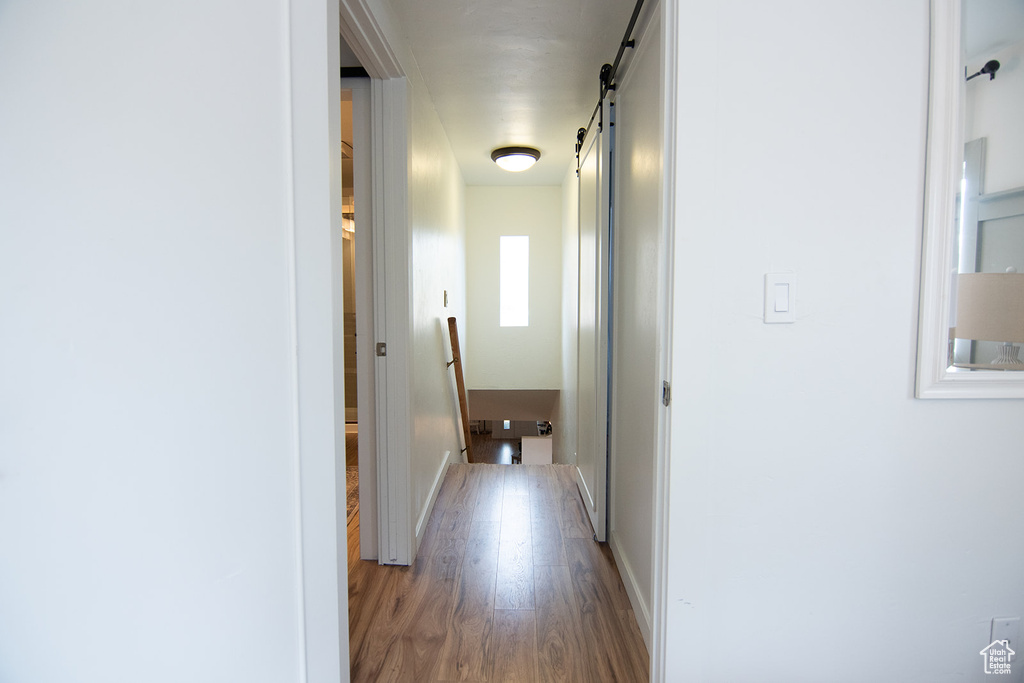 Corridor with a barn door, wood finished floors, an upstairs landing, and baseboards