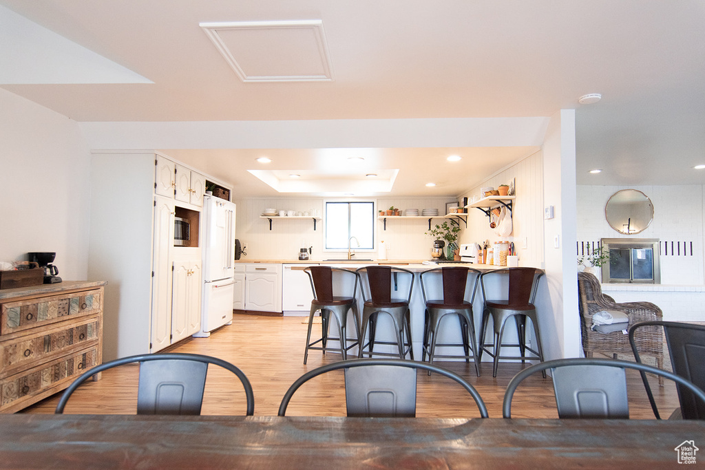 Kitchen with open shelves, light wood-style flooring, white appliances, a kitchen breakfast bar, and light countertops