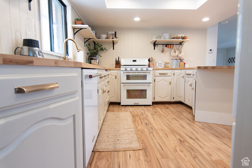 Kitchen featuring range with two ovens, open shelves, light wood finished floors, white cabinets, and a sink