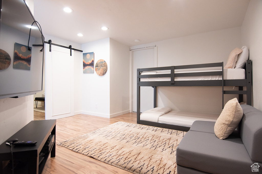 Bedroom with a barn door, light wood finished floors, recessed lighting, and baseboards