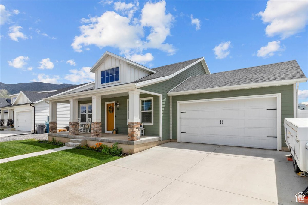 View of front of home with board and batten siding, covered porch, concrete driveway, an attached garage, and a mountain view
