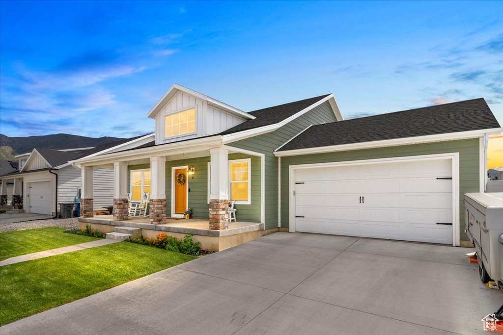 View of front of property featuring covered porch, a garage, driveway, board and batten siding, and roof with shingles