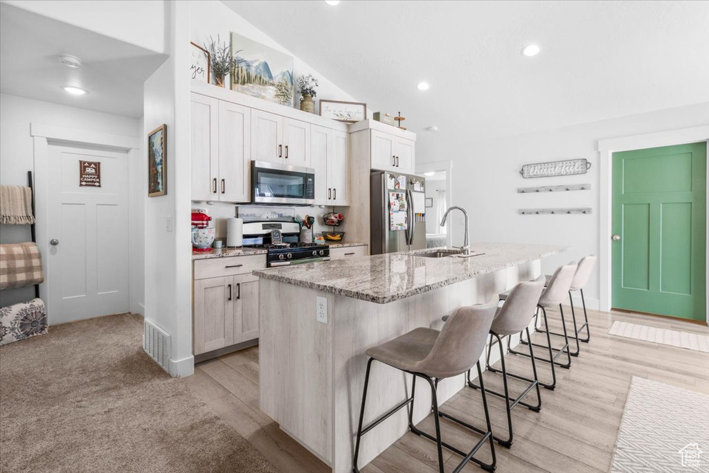 Kitchen featuring appliances with stainless steel finishes, a sink, a center island with sink, a breakfast bar, and light stone countertops