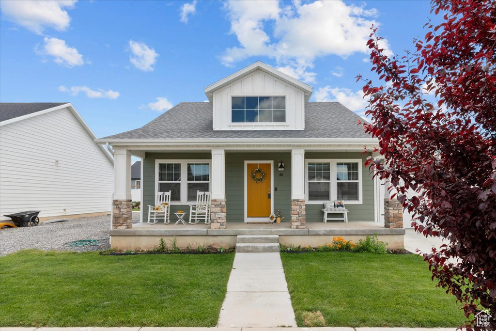 Craftsman-style home featuring covered porch, stone siding, a front yard, and roof with shingles