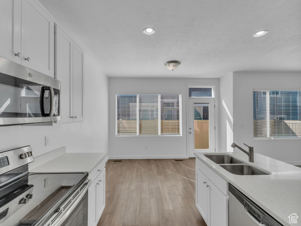 Kitchen featuring appliances with stainless steel finishes, a sink, white cabinetry, light wood-style flooring, and recessed lighting