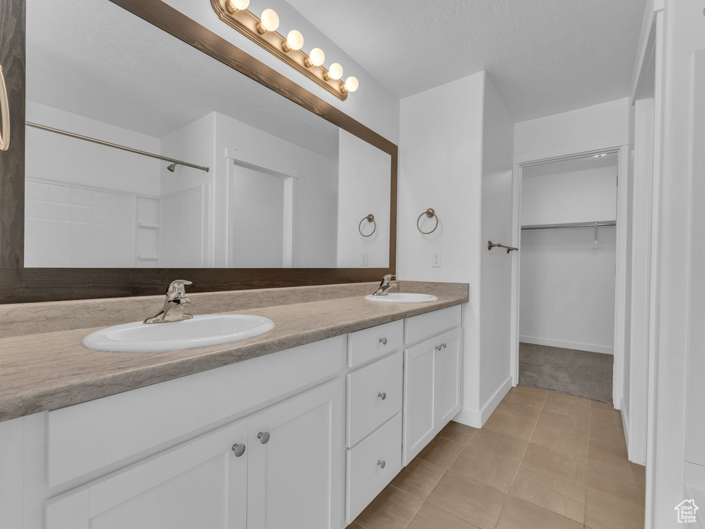Full bath featuring double vanity, a walk in closet, and baseboards