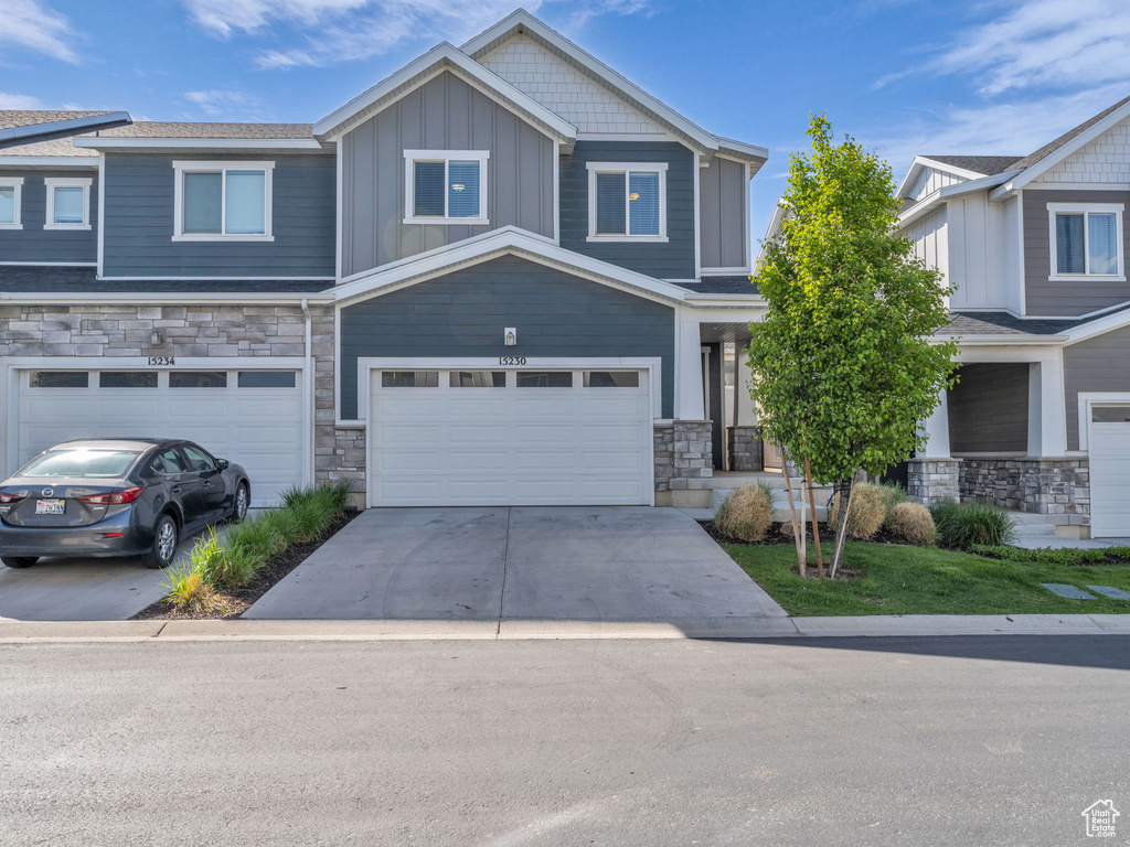 View of front facade featuring stone siding, concrete driveway, an attached garage, and board and batten siding