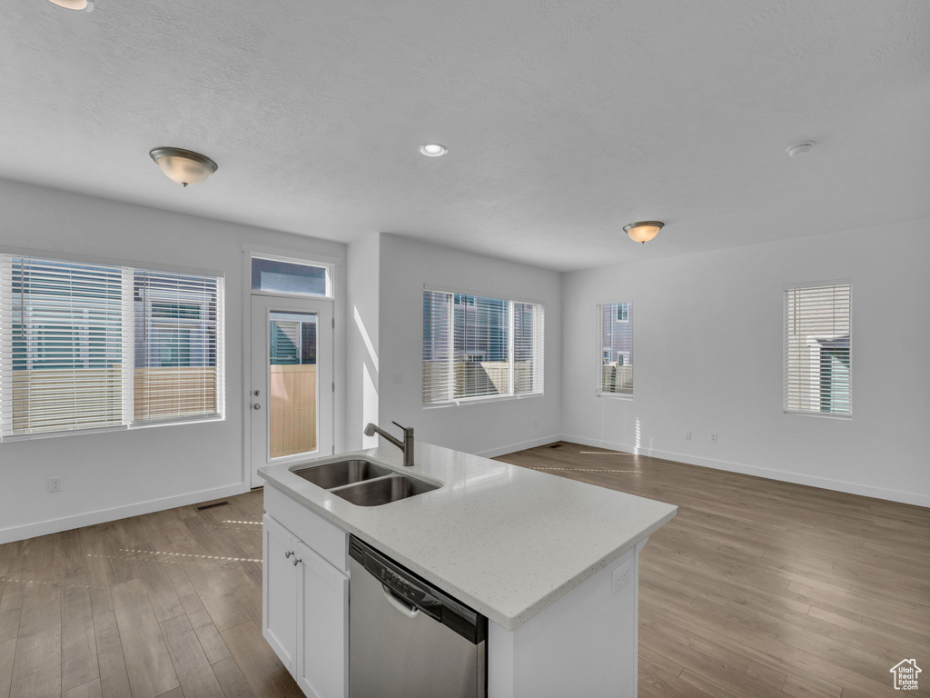 Kitchen with dishwasher, a sink, wood finished floors, white cabinetry, and baseboards