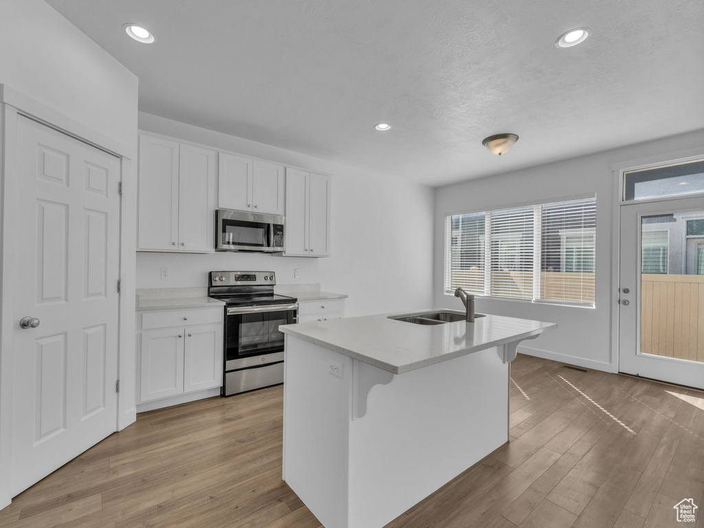 Kitchen featuring appliances with stainless steel finishes, a sink, white cabinetry, light wood-style flooring, and recessed lighting