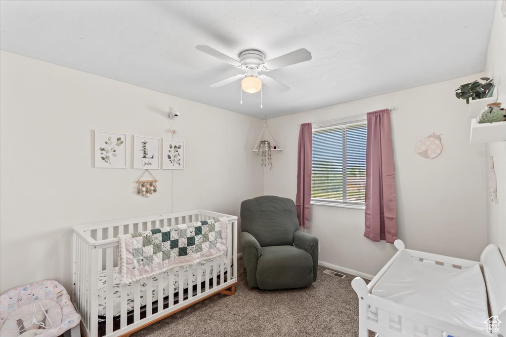 Bedroom featuring a crib, carpet flooring, a ceiling fan, and baseboards