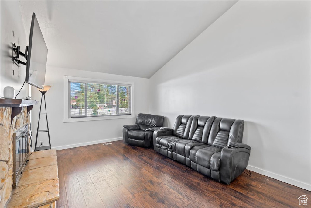 Living area featuring vaulted ceiling, hardwood / wood-style floors, baseboards, and a stone fireplace