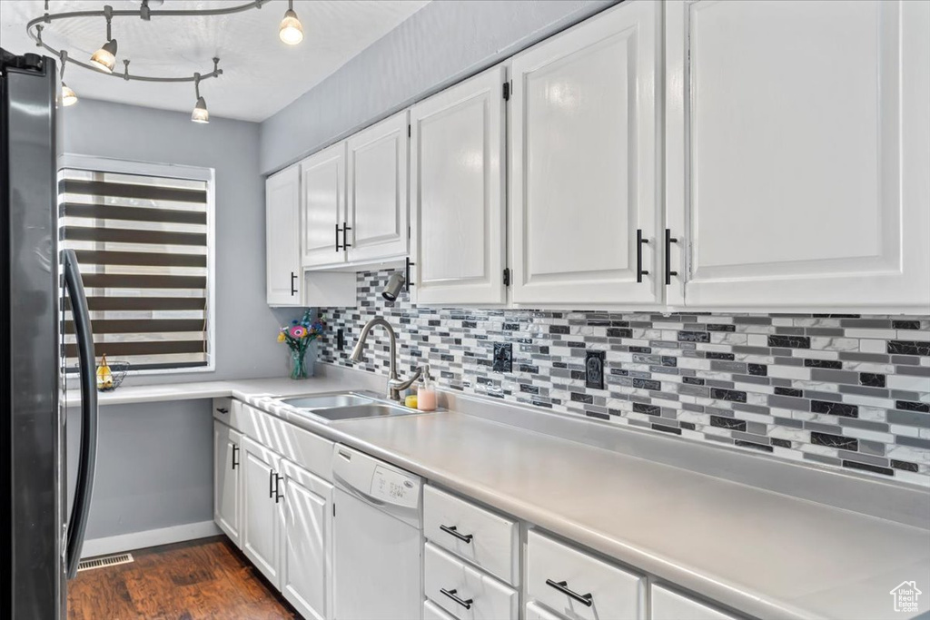 Kitchen with white dishwasher, a sink, tasteful backsplash, and white cabinets