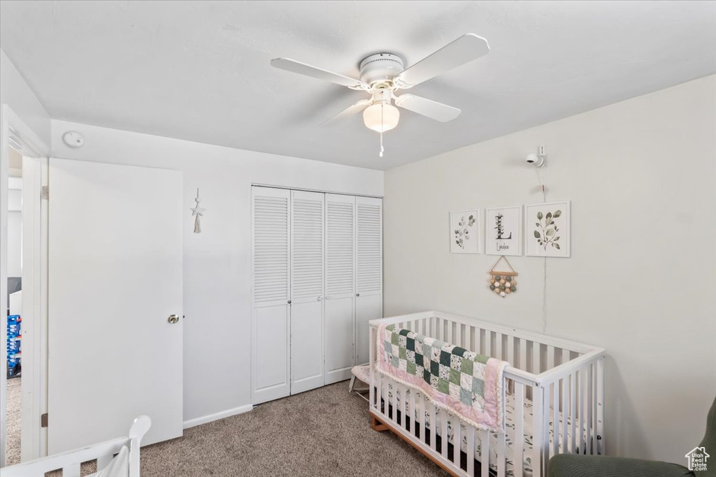 Carpeted bedroom with a closet, a crib, and ceiling fan