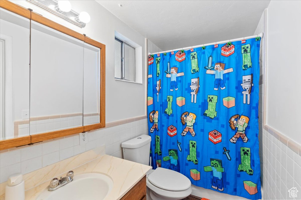 Full bath featuring tile walls, toilet, a shower with curtain, vanity, and a wainscoted wall