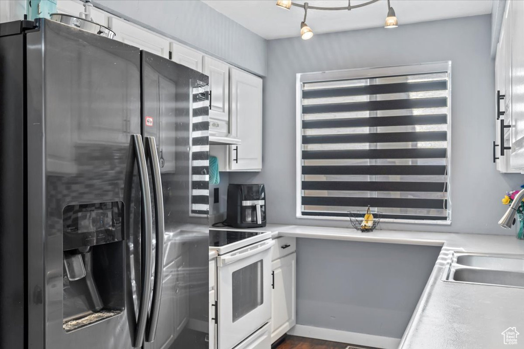 Kitchen with stainless steel fridge with ice dispenser, white range with electric cooktop, white cabinetry, light countertops, and a sink