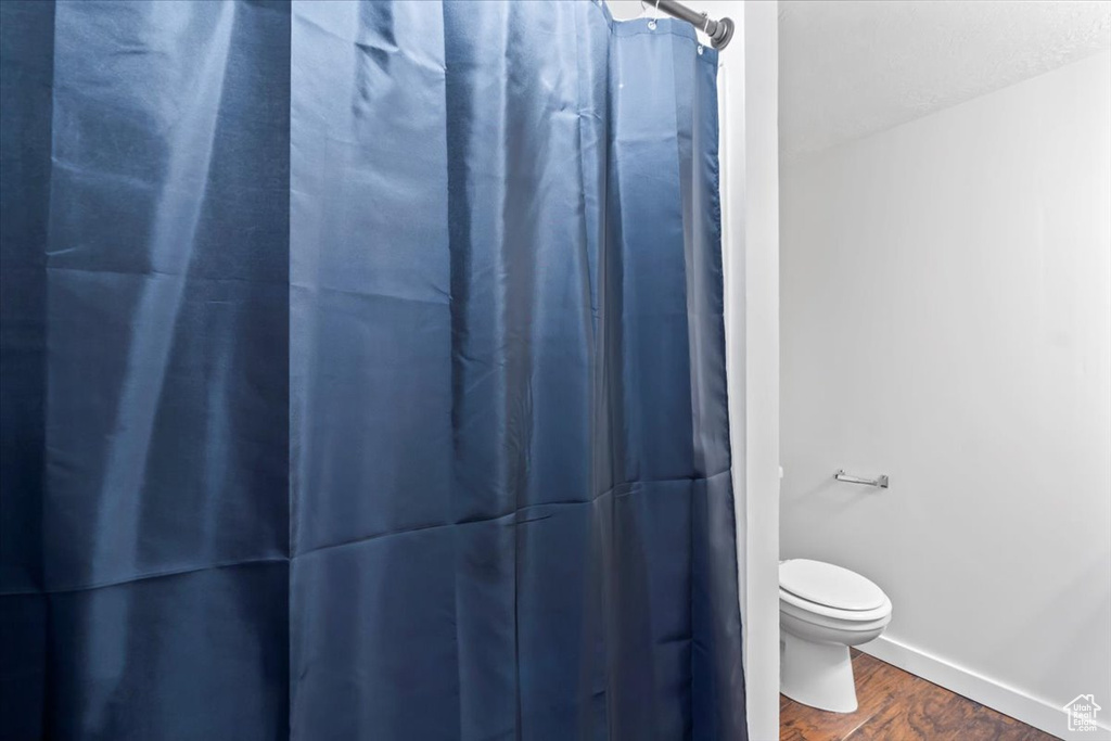 Full bath with wood finished floors, toilet, curtained shower, and baseboards