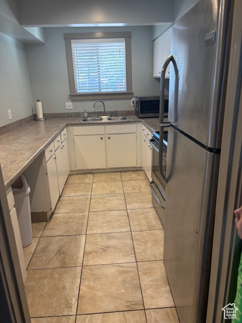 Kitchen featuring appliances with stainless steel finishes, a sink, light tile patterned floors, and white cabinets