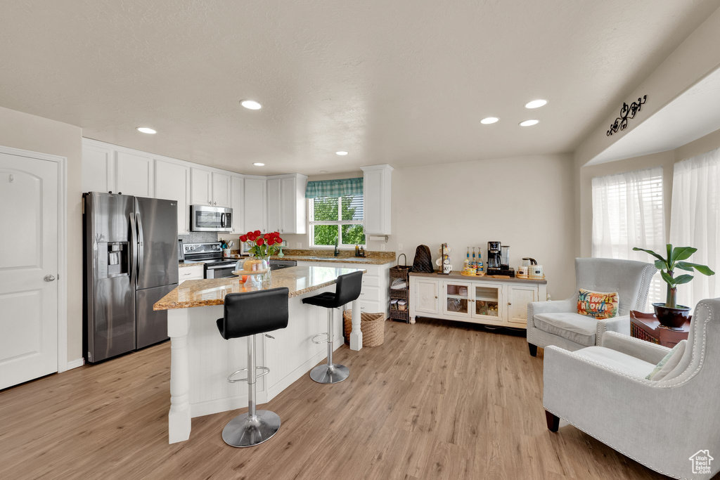 Kitchen with appliances with stainless steel finishes, a breakfast bar, light wood finished floors, white cabinetry, and recessed lighting