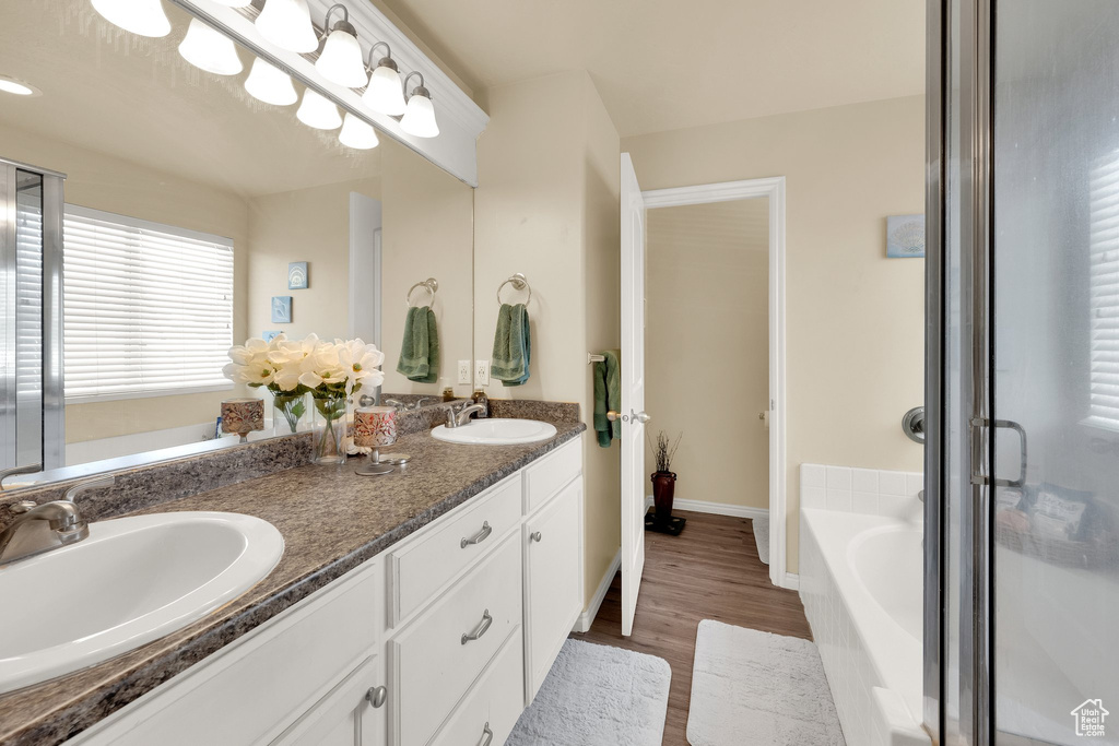 Bathroom featuring wood finished floors, a bath, double vanity, a shower stall, and baseboards
