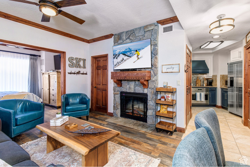 Living area with a fireplace, ceiling fan, ornamental molding, a textured ceiling, and light wood-type flooring