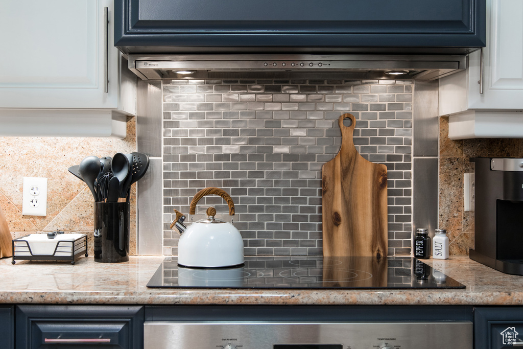 Kitchen view of backsplash, black electric cooktop, oven, and white cabinetry