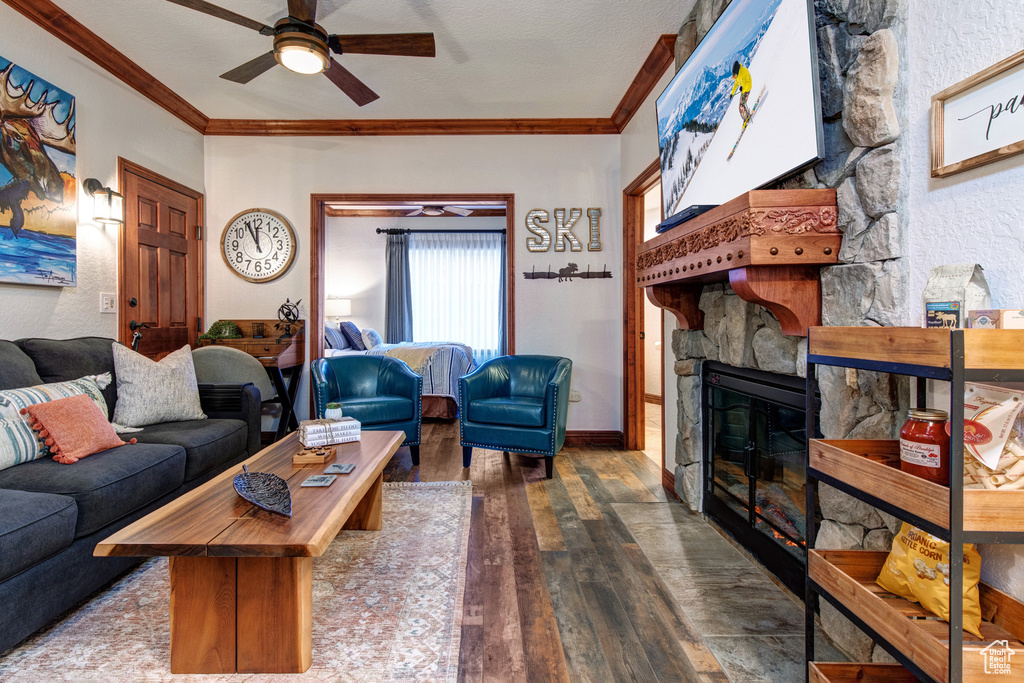 Living area with a ceiling fan, crown molding, hardwood / wood-style floors, a stone fireplace, and baseboards