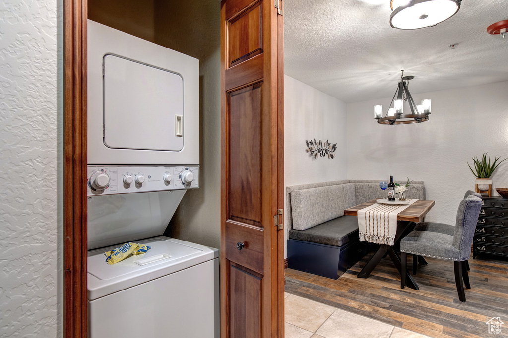 Clothes washing area with stacked washing machine and dryer, a chandelier, a textured ceiling, light wood-style flooring, and a textured wall