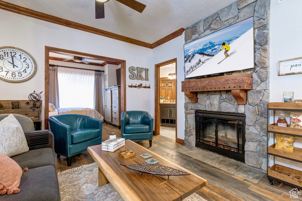Living room with a ceiling fan, crown molding, a fireplace, wood finished floors, and a textured ceiling