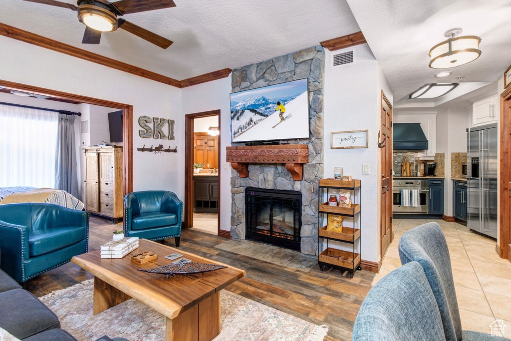 Living room with a ceiling fan, a stone fireplace, ornamental molding, and a textured ceiling