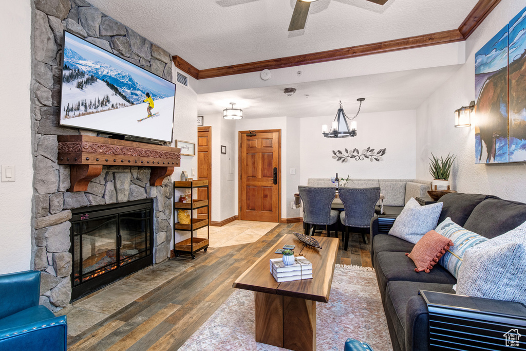 Living room featuring wood finished floors, a fireplace, a chandelier, crown molding, and ceiling fan