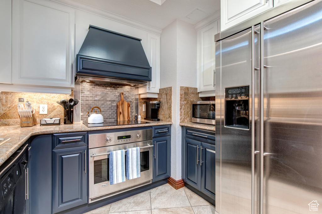 Kitchen featuring appliances with stainless steel finishes, custom range hood, blue cabinets, and white cabinets