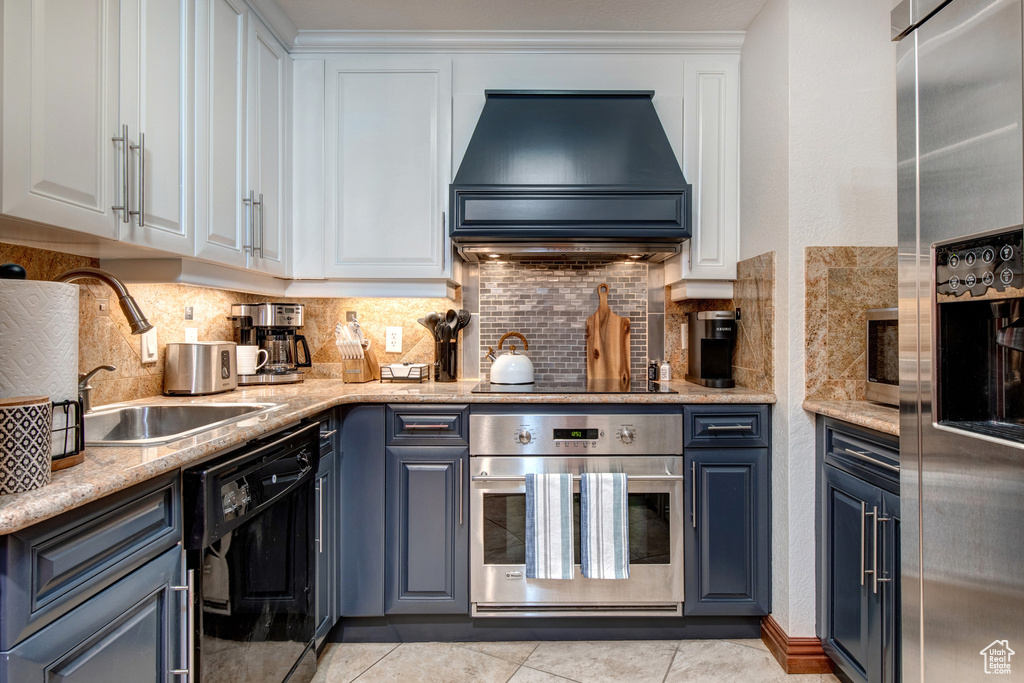 Kitchen featuring appliances with stainless steel finishes, custom range hood, decorative backsplash, white cabinetry, and a sink