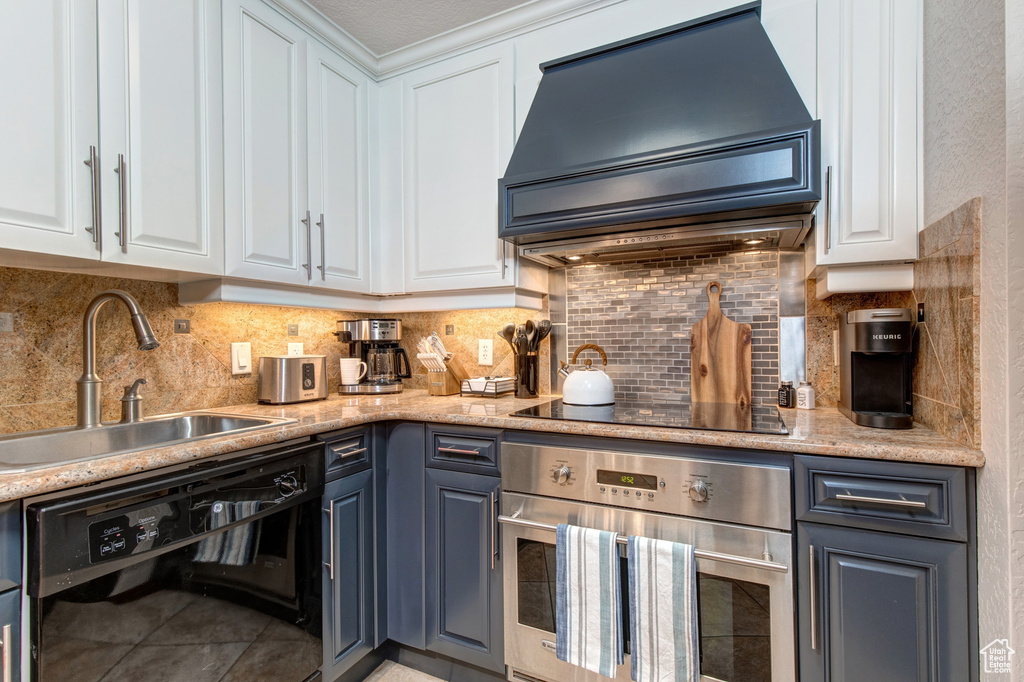 Kitchen with black appliances, custom range hood, a sink, and white cabinets