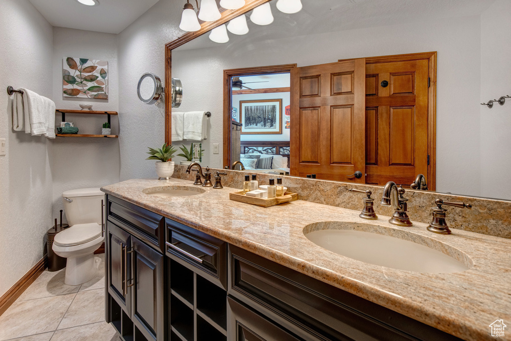 Bathroom featuring toilet, double vanity, tile patterned floors, baseboards, and ceiling fan