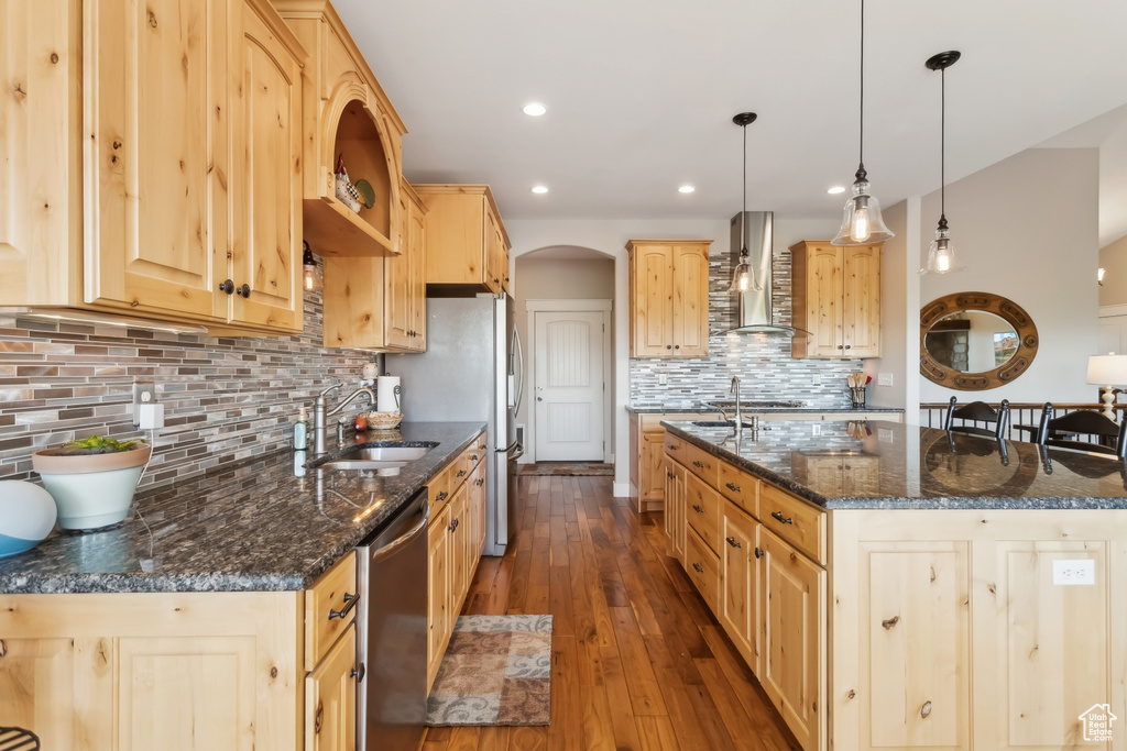 Kitchen with stainless steel appliances, a sink, wall chimney range hood, arched walkways, and backsplash