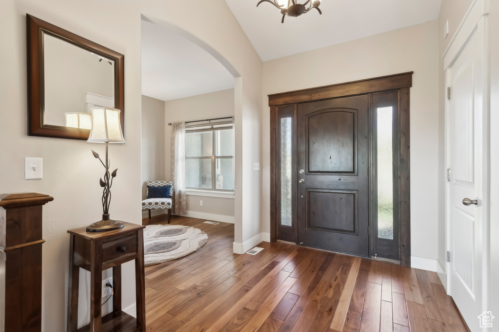 Foyer entrance featuring arched walkways, baseboards, wood-type flooring, and vaulted ceiling