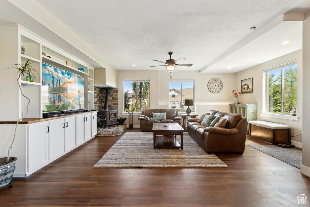 Living area featuring a wood stove, healthy amount of natural light, dark wood-style flooring, ceiling fan, and recessed lighting
