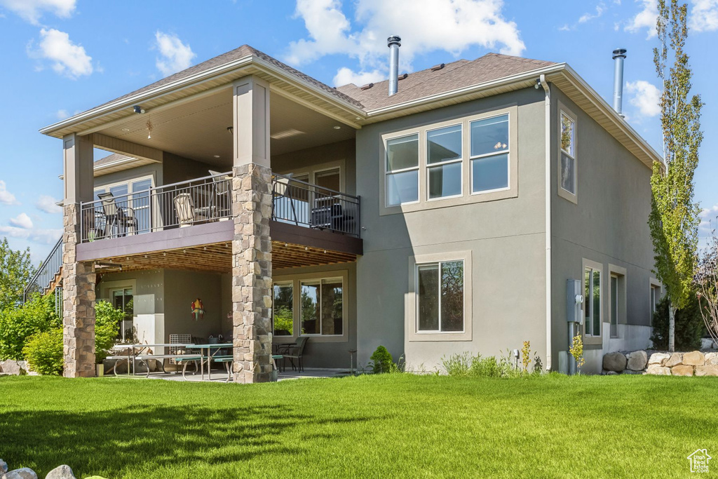 Back of house featuring stucco siding, a lawn, a patio area, and a balcony