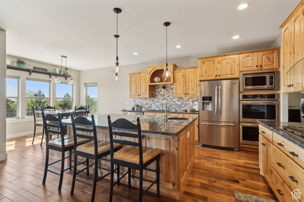 Kitchen with appliances with stainless steel finishes, light brown cabinets, a sink, a breakfast bar area, and dark wood-style flooring