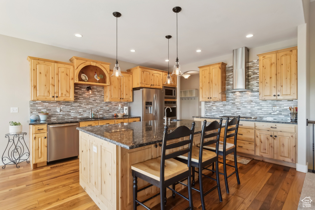 Kitchen with appliances with stainless steel finishes, wall chimney range hood, light brown cabinetry, and recessed lighting
