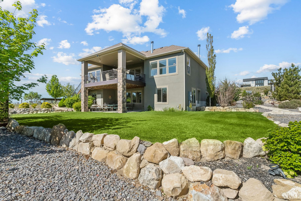 Back of house with a balcony, stucco siding, a yard, and a patio area