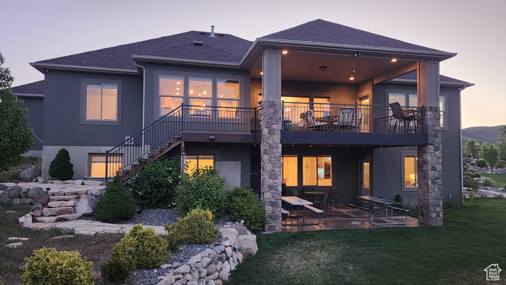 Back of house at dusk with stucco siding, a patio, stairs, and a lawn