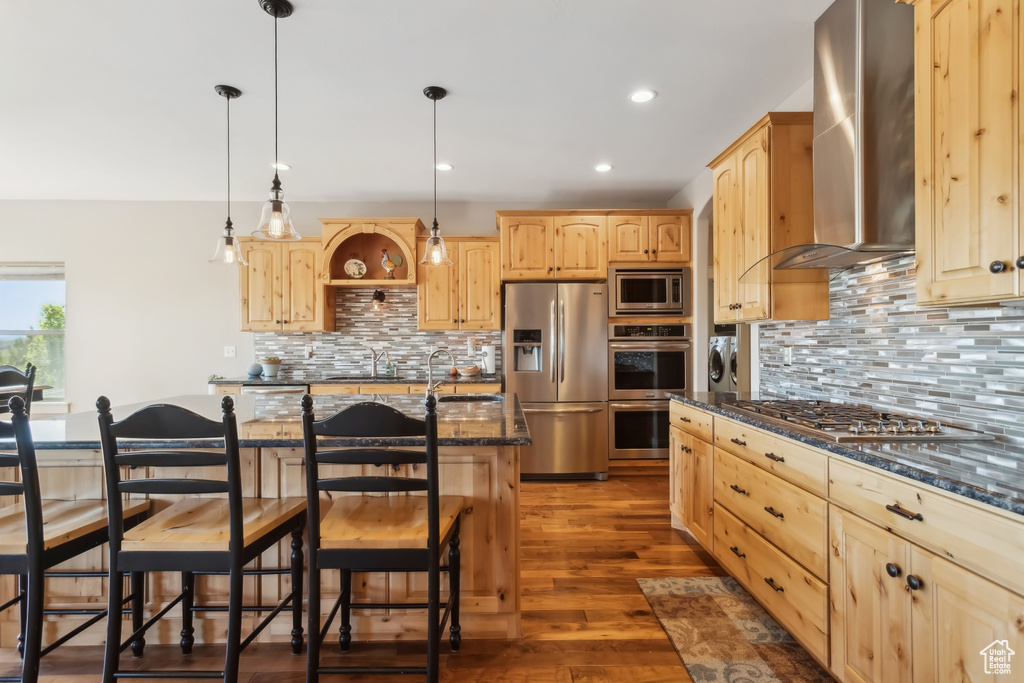 Kitchen with stainless steel appliances, light brown cabinetry, wall chimney range hood, independent washer and dryer, and backsplash