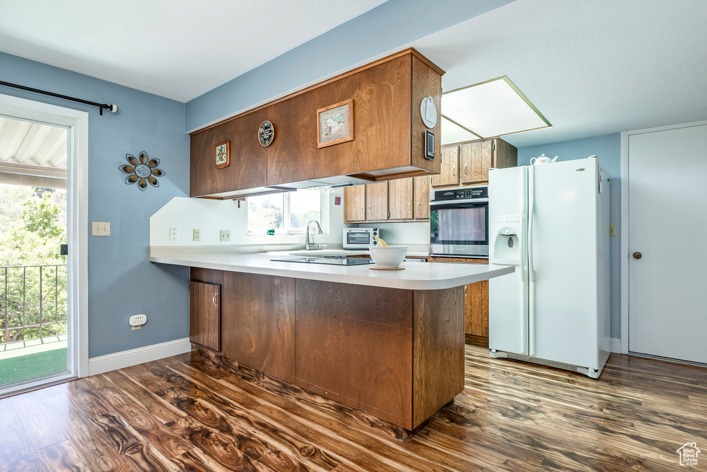 Kitchen with white refrigerator with ice dispenser, oven, dark wood-type flooring, a peninsula, and light countertops