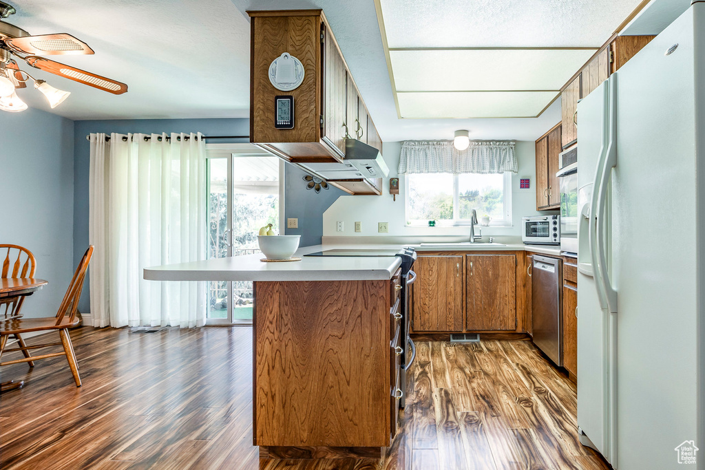 Kitchen featuring white refrigerator with ice dispenser, brown cabinetry, dishwasher, a sink, and a peninsula